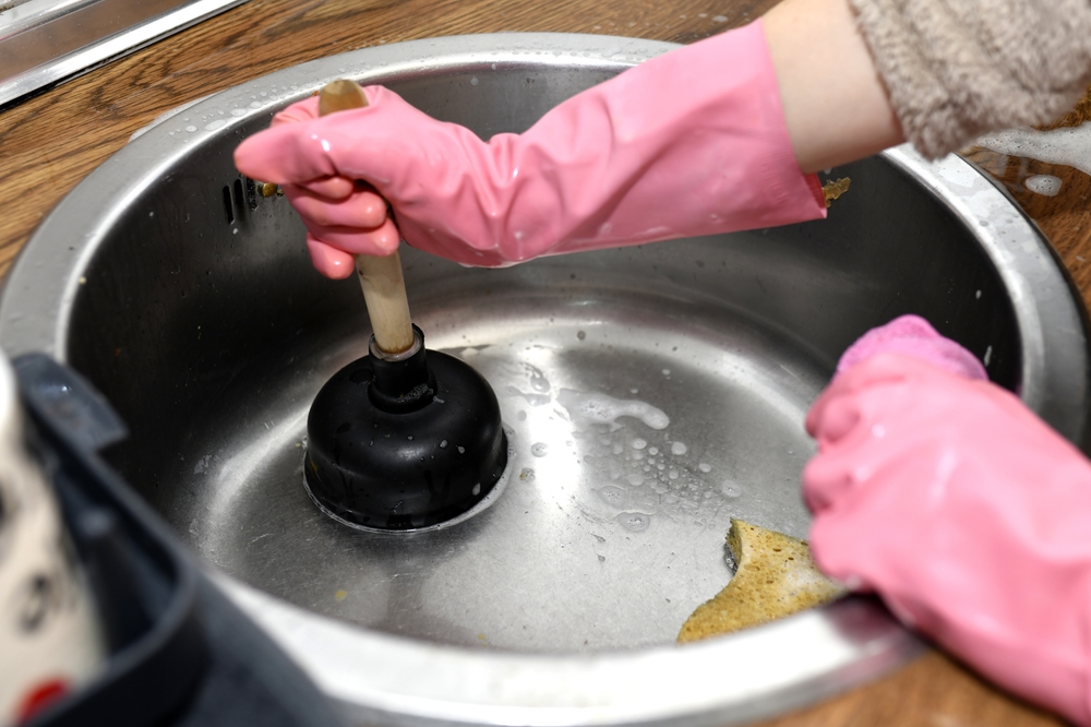 Woman's Hands With A Plunger Unclogging The Kitchen Drain